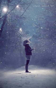 a woman standing in the snow with her hands on her hips looking up at something