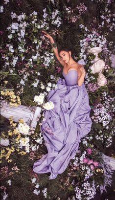 a woman in a purple dress laying on the ground surrounded by wildflowers and other flowers