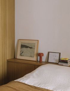 a bed with white sheets and pillows in a bedroom next to a wooden dresser, framed pictures on the wall