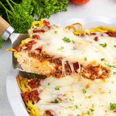 two pieces of lasagna with meat and cheese in a white dish next to parsley