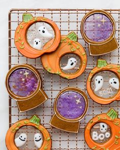 halloween cookies decorated like pumpkins and ghost heads on a cooling rack with candy in them