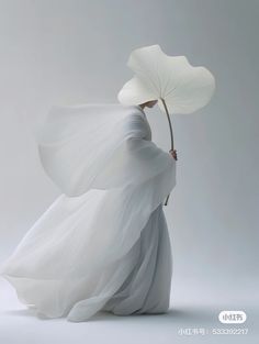 a woman in a white dress holding a large leaf with her back to the camera