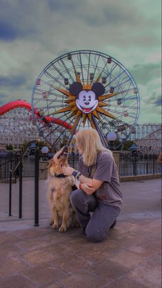 a person kneeling down petting a dog in front of a ferris wheel