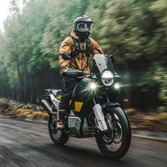 a man riding on the back of a motorcycle down a forest road with trees in the background