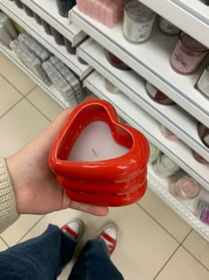 a person holding a heart shaped candle in front of shelves filled with jars and candles