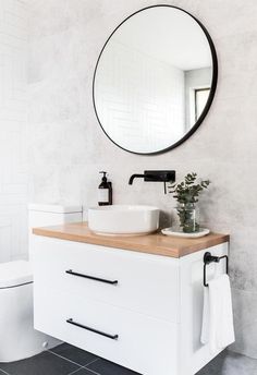 a white bathroom with a round mirror above the sink and a wooden counter top below it