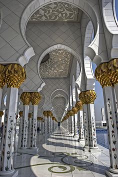 the inside of a building with columns and arches on each side, lined with gold - trimmed pillars