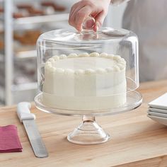 a person is decorating a cake with icing on a glass platter that sits on a wooden table