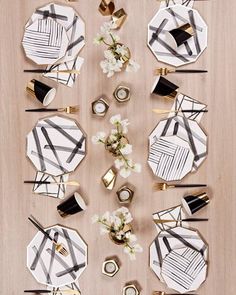 the table is set with black and white plates, napkins, gold candles and flowers