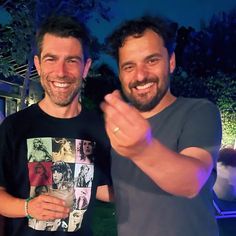 two men standing next to each other in front of a house at night with their hands together