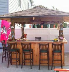 an outdoor bar with stools and tables in front of a fenced off house