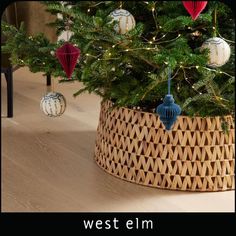 a christmas tree with ornaments hanging from it's branches in a basket on the floor