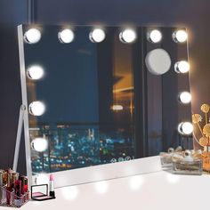 a vanity mirror with lights on top of it next to makeup brushes and lipstick in front of a window