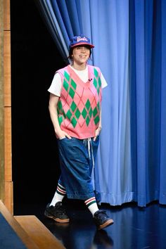 a man standing on top of a stage in front of a blue curtain wearing a hat