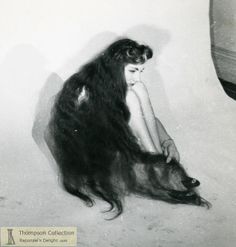 an old photo of a woman with long hair sitting on the floor next to a wall