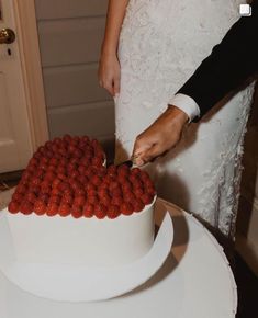 a newly married couple cutting their wedding cake with strawberries on top and the bride is wearing a white dress