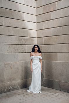 a woman standing in front of a wall wearing a white dress