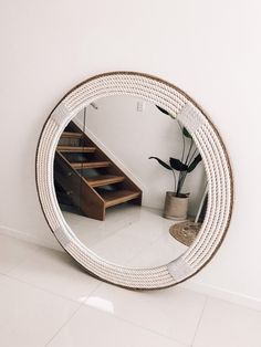 a round mirror sitting on top of a white floor next to a plant and stairs