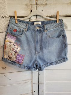 a pair of jean shorts with patches on them hanging up against a white wooden wall