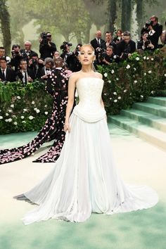 a woman in a white dress standing on a green carpet with people behind her and taking pictures