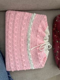 a knitted pink hat sitting on top of a couch next to a pair of jeans