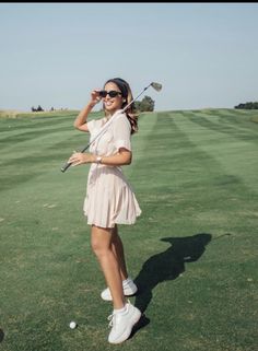 a woman standing on top of a lush green field holding a golf racquet