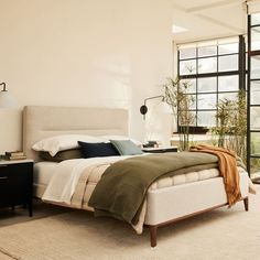 a bedroom with a bed, nightstands and plants in the window sill next to it