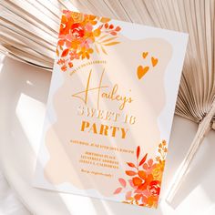 an orange and yellow floral themed party card on a white plate with fan in the background