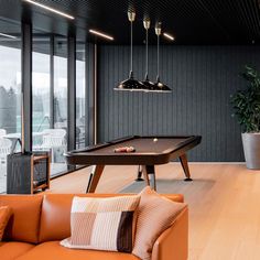 a pool table in the middle of a living room with couches and lamps hanging from the ceiling