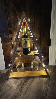 a bottle and two glasses sitting in front of a wooden triangle with lights on it