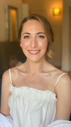 a woman in white shirt sitting on bed smiling at the camera with her eyes closed