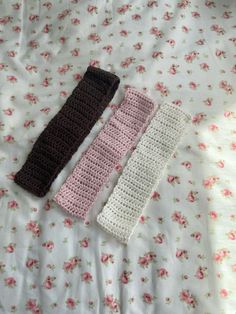 three crocheted headbands laying on top of a floral bed sheet with pink and white flowers