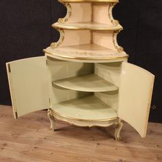 an antique corner cabinet with gold trimmings on the top and bottom, has three shelves