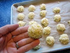 a hand is holding something in front of a baking sheet with balls of food on it