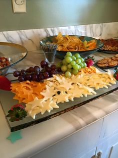 an assortment of cheeses, fruit and crackers on a marble countertop in a kitchen