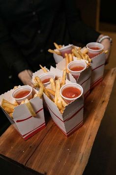 french fries with ketchup and mustard are on a wooden tray in front of a man