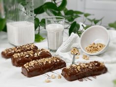 three pieces of chocolate with nuts and milk on a table next to some glassware