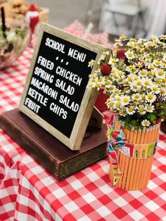 a table topped with a sign and flowers next to a potted plant on top of a book