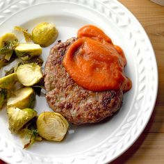 a white plate topped with a hamburger covered in sauce next to brussel sprouts