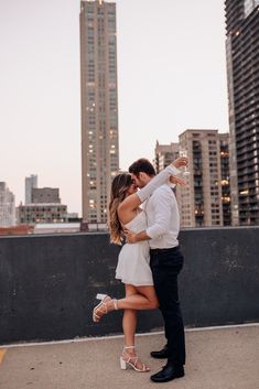 a man and woman standing next to each other in front of tall buildings with their arms around each other