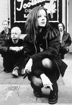 black and white photograph of woman crouching on sidewalk in front of store with men