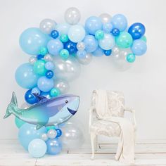 a shark balloon arch next to a chair with balloons on the wall and a white chair