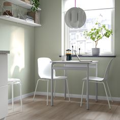 two white chairs sitting at a table with a potted plant in the window sill