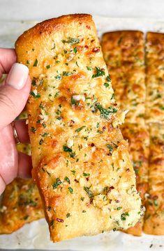 a person holding up a piece of bread with cheese and herbs