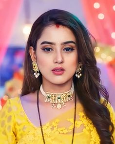 a woman in yellow dress with necklaces and earrings on her neck, looking at the camera