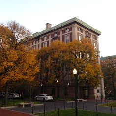 an old building is surrounded by trees with yellow leaves on the tops and green roof