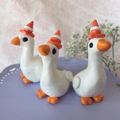 three white ducks wearing orange hats on top of a blue table next to some flowers