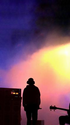 the silhouette of a person standing next to a guitar in front of a purple and yellow sky