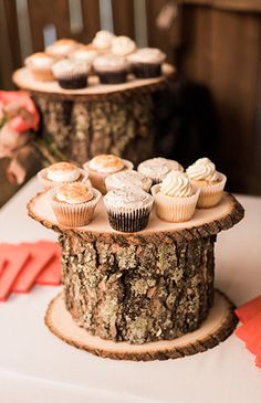 cupcakes are sitting on top of a tree stump at a wedding reception in the woods