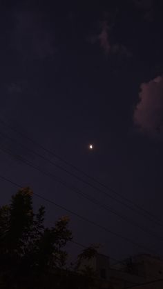 the moon is shining brightly in the night sky over some trees and power lines,